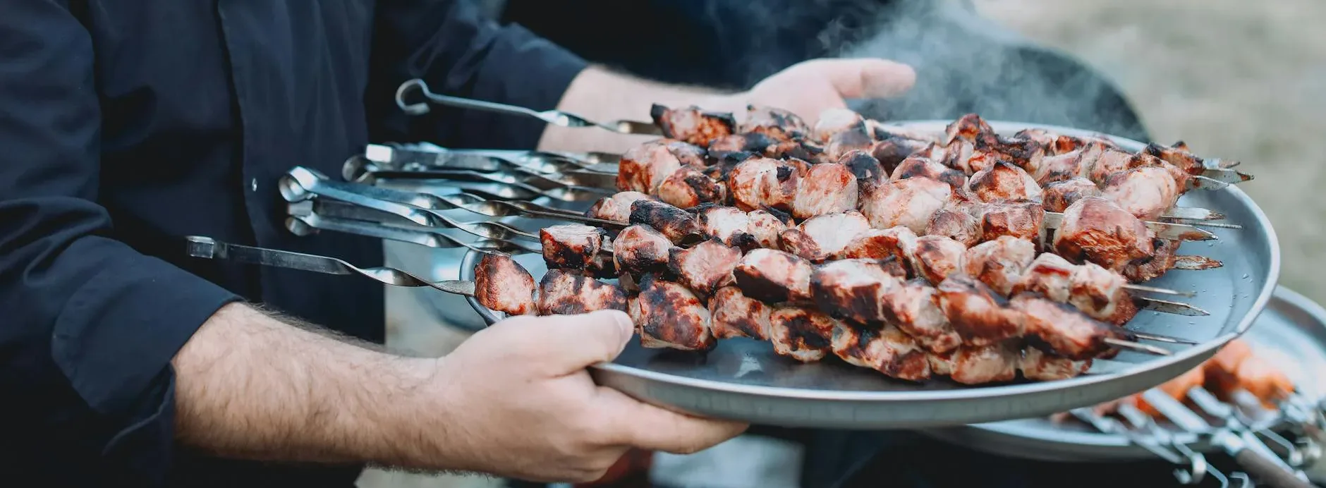 close up of a man holding a tray with grilled meat